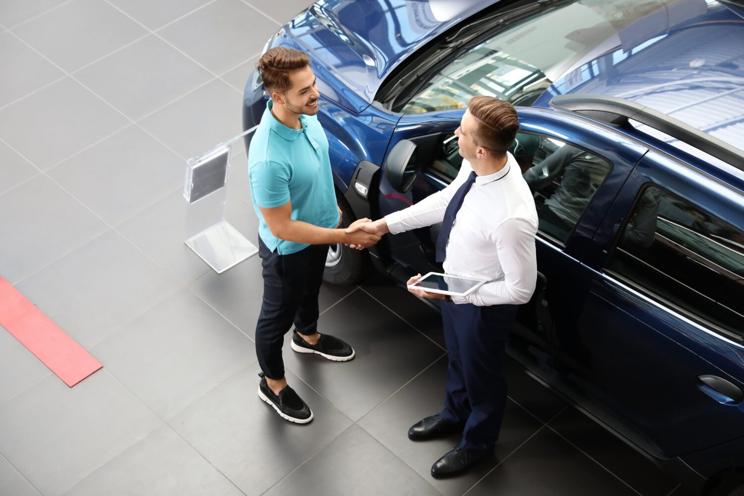 Young car salesman shaking hands with client in dealership